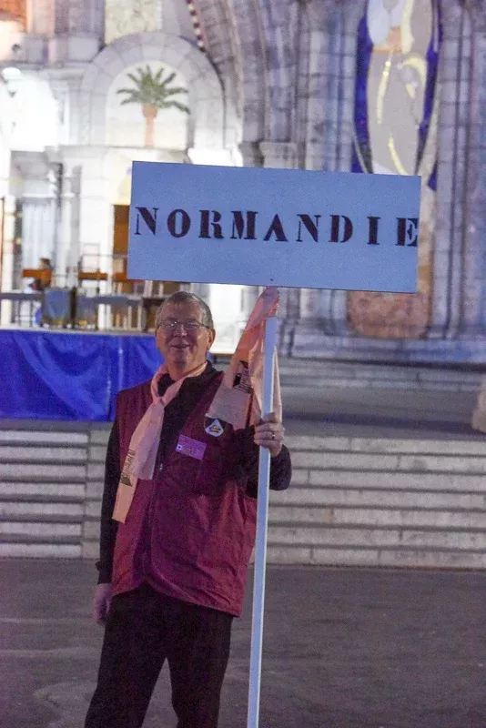 Homme tenant pancarte Normandie devant un bâtiment.