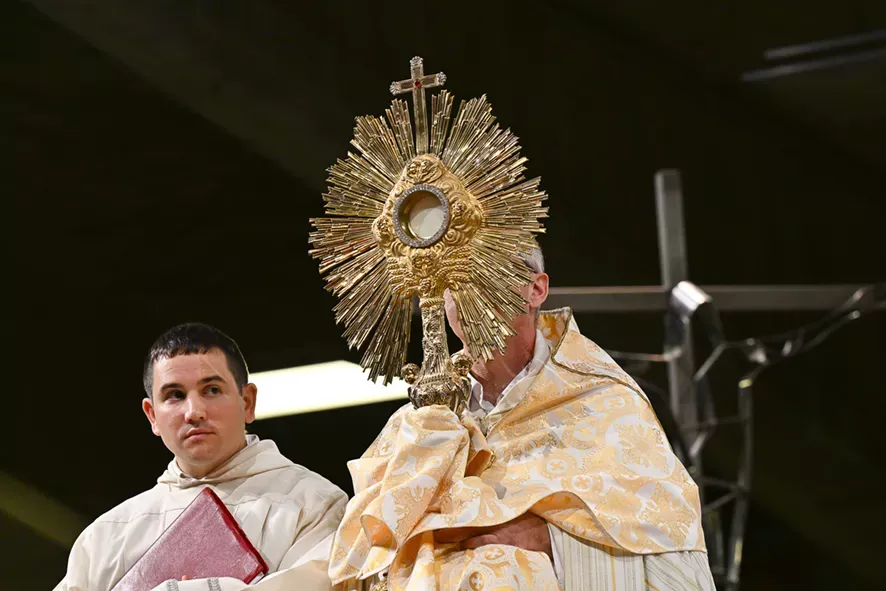 Prêtre portant un ostensoir doré lors d'une cérémonie religieuse.