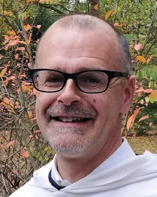 Portrait d'un homme souriant avec des lunettes et un collier.