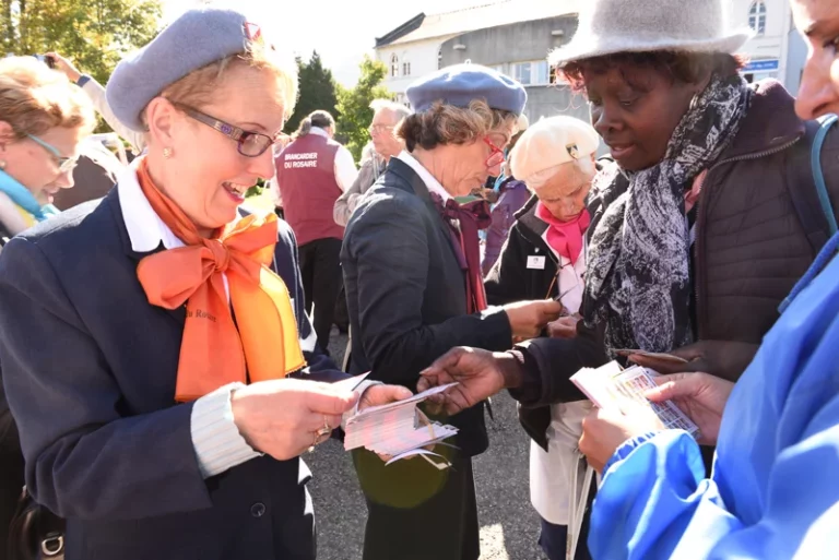 Plusieurs femmes, dont des bénévoles du Rosaire en uniforme, échangent des cartes ou des documents lors d'un rassemblement en extérieur.
