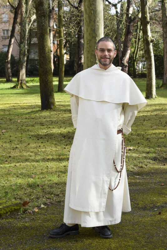 Homme religieux souriant en froc blanc et chapelet dans un parc arboré