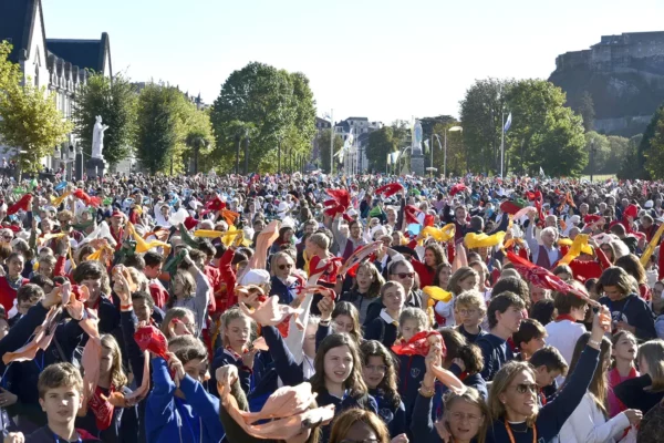 Grande foule de jeunes pèlerins à Lourdes agitant des foulards colorés près de la basilique